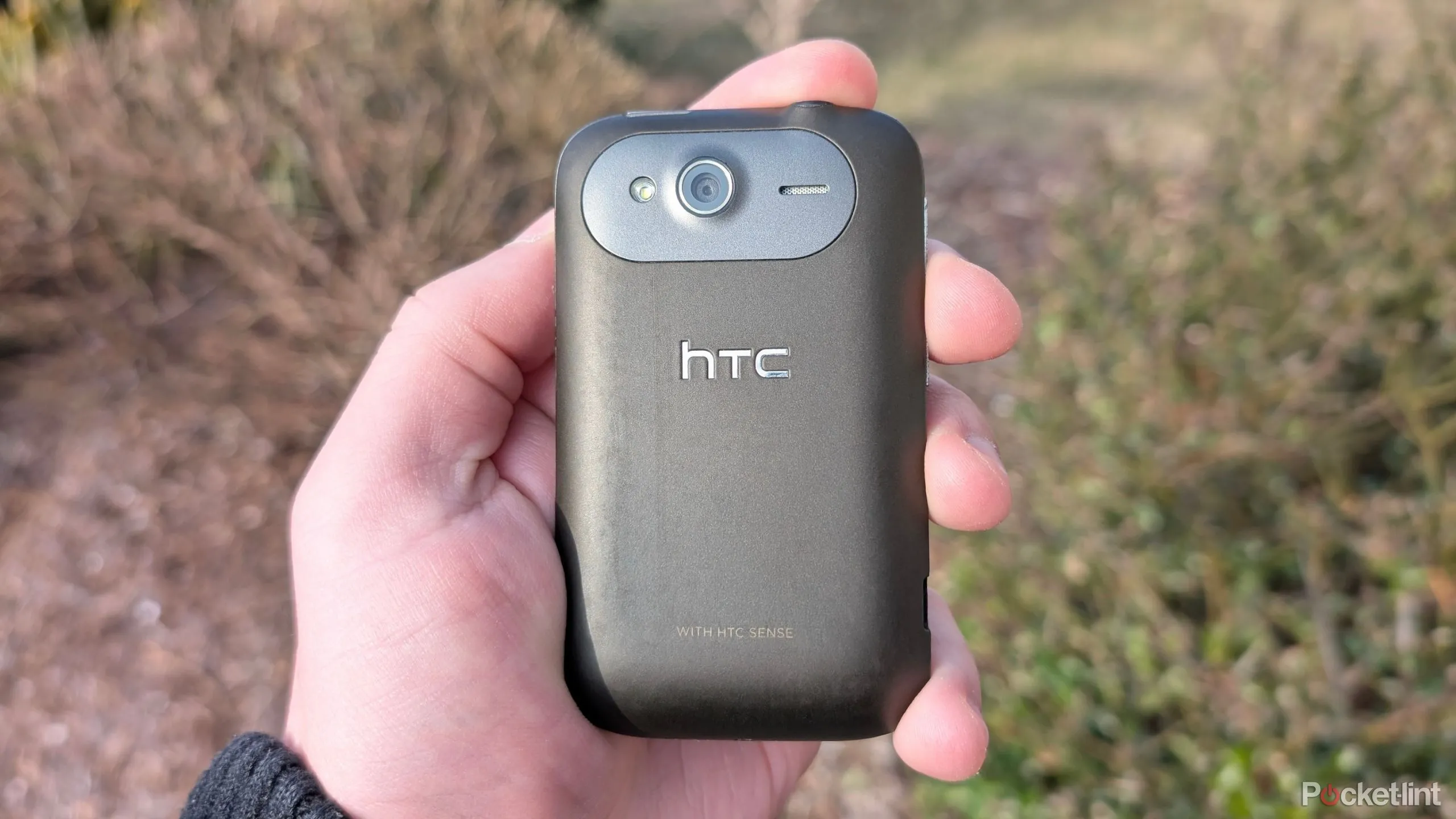 Chiếc điện thoại HTC Wildfire S màu đen đặt trên bề mặt gỗ