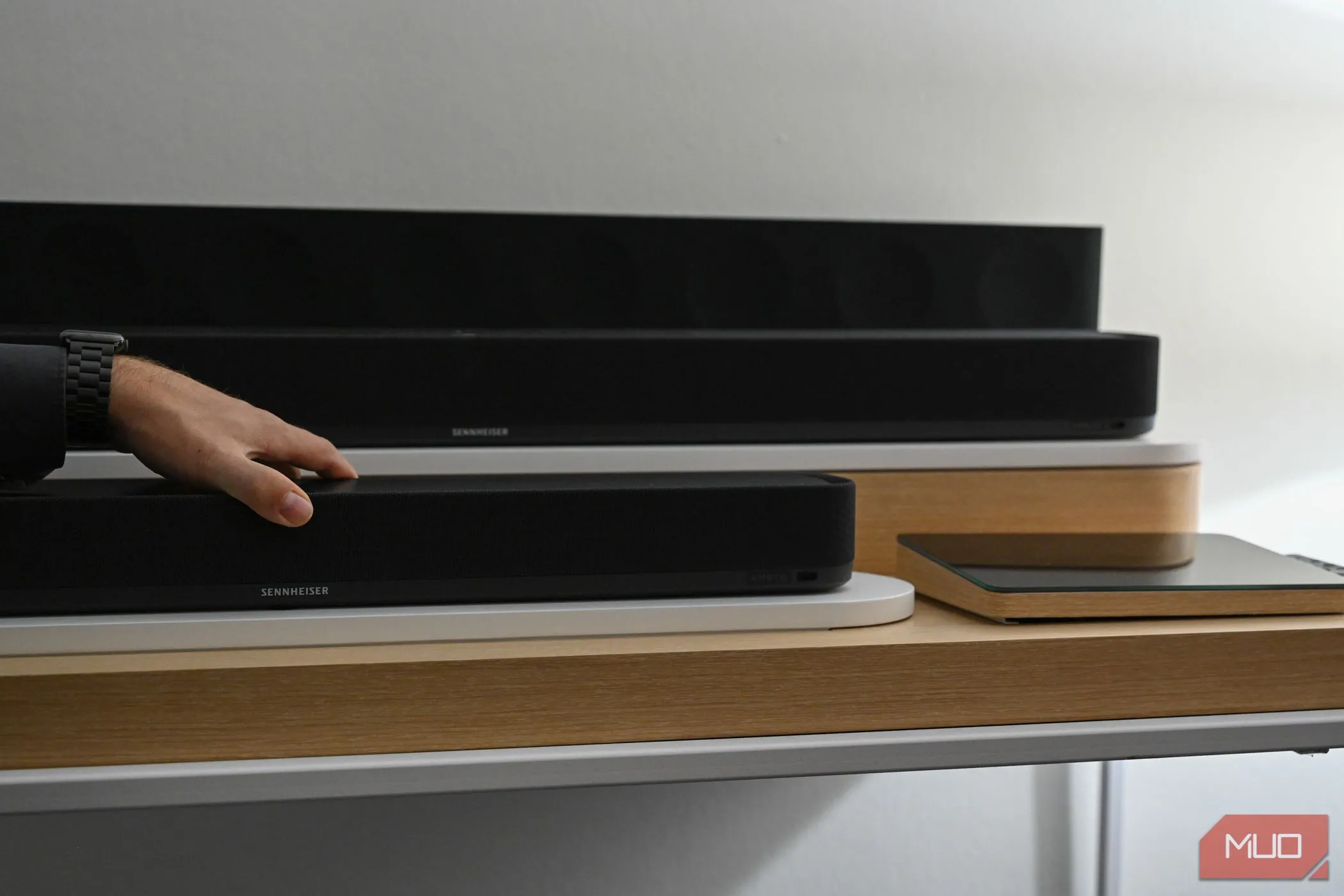 Bàn tay chạm vào loa soundbar Sennheiser Ambeo Mini màu đen.