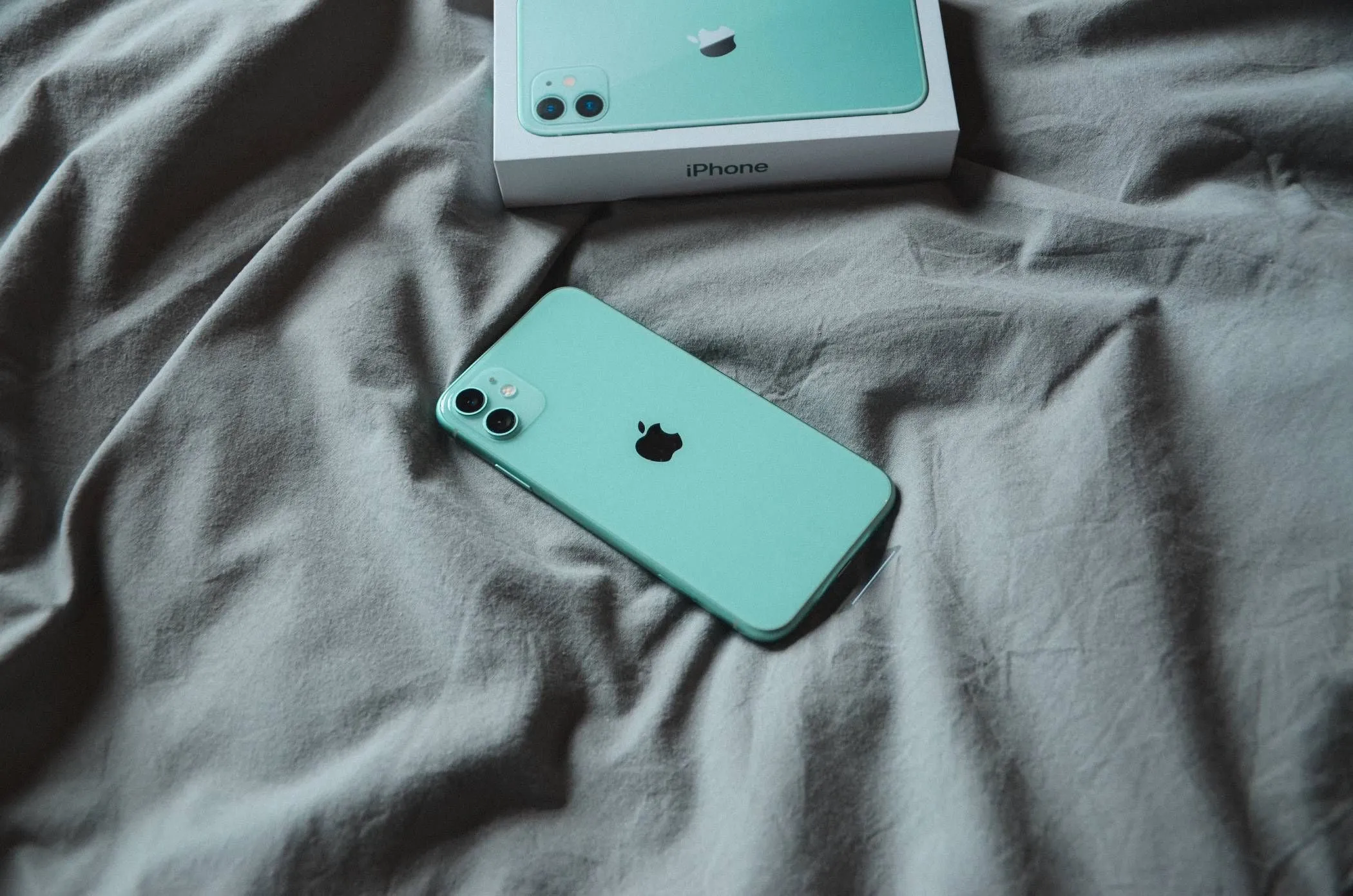 Chiếc iPhone đang nằm trên chăn ga trải giường trong khi sạc, cảnh báo về nguy cơ tích nhiệt và ảnh hưởng xấu đến pin.