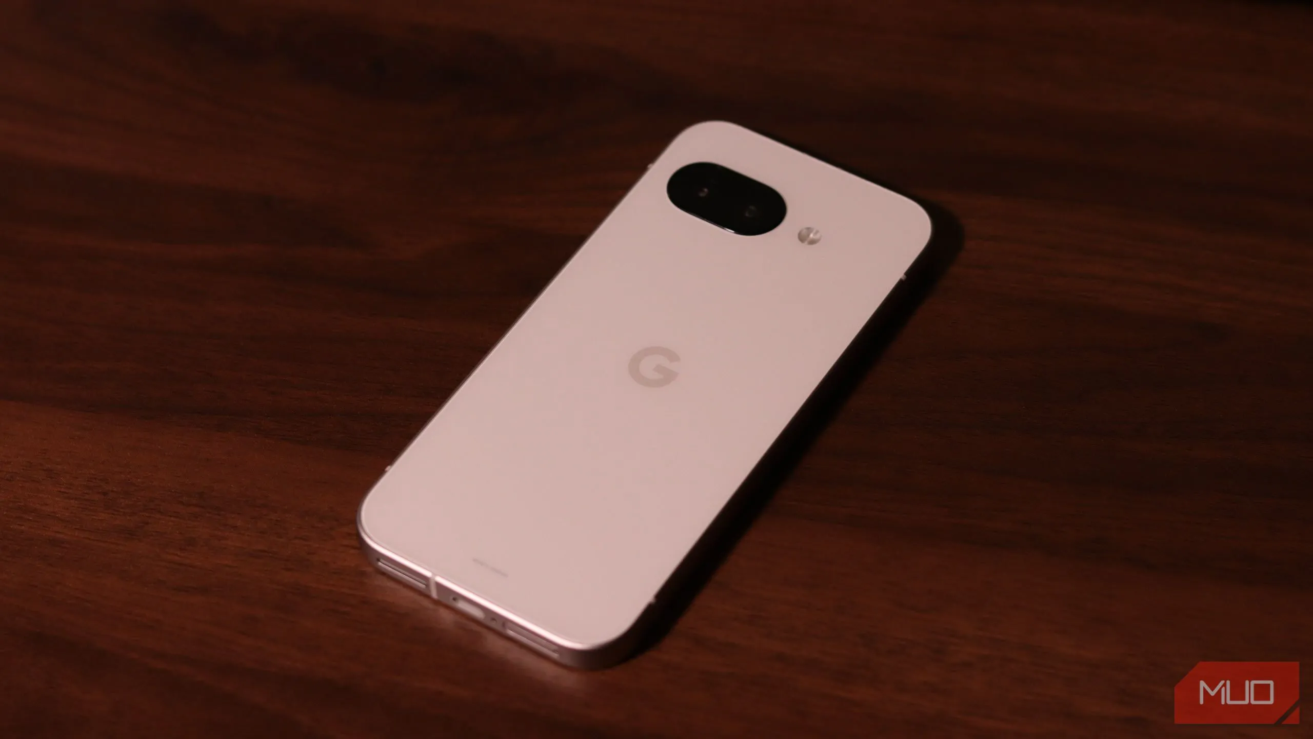 Điện thoại Google Pixel 9a màu xanh lá cây đặt trên bề mặt gỗ, mặt lưng hướng lên.