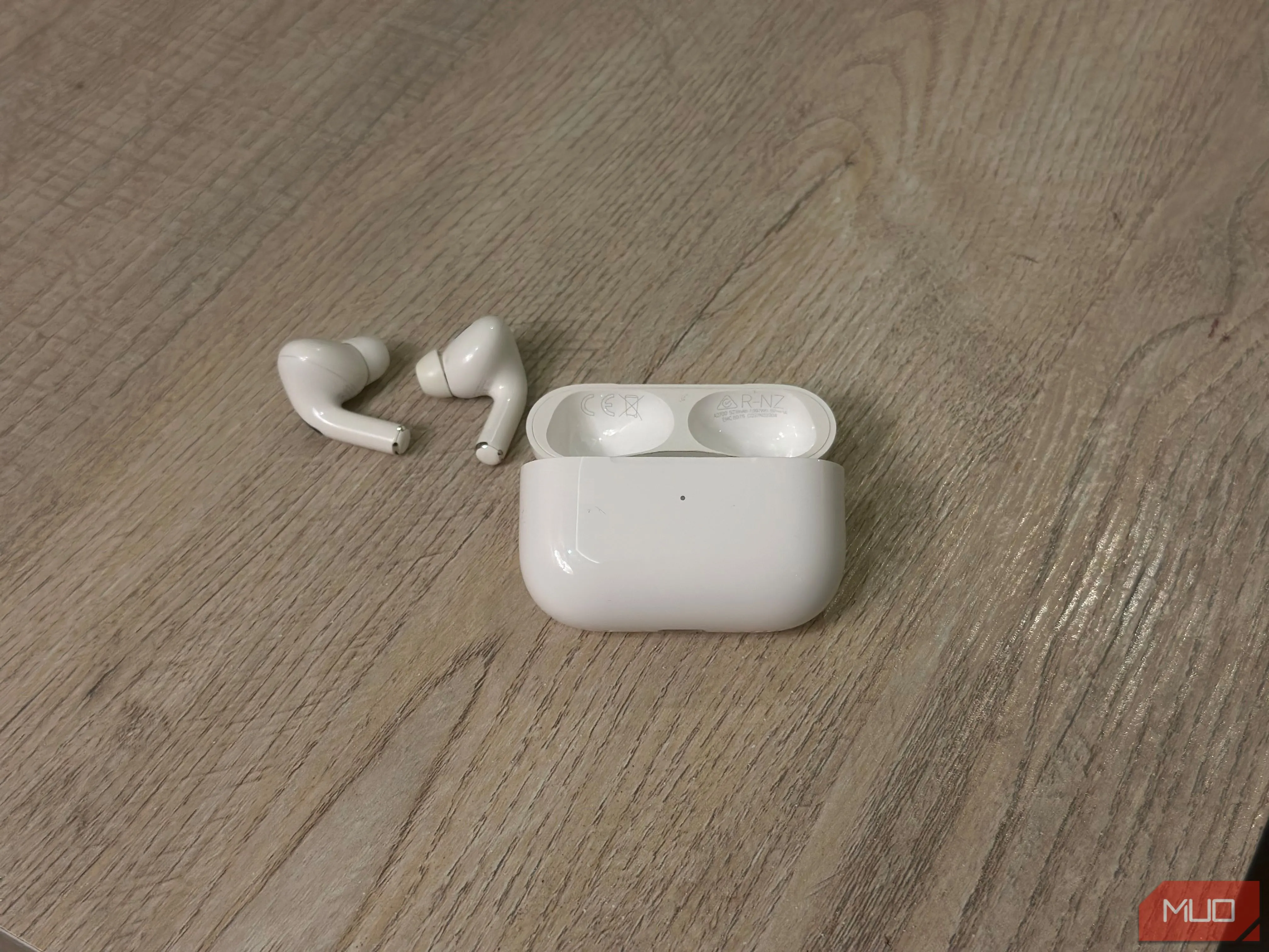 Hộp sạc AirPods và tai nghe nằm trên mặt bàn, minh họa vị trí số kiểu máy và số sê-ri được in bên trong nắp hộp sạc.