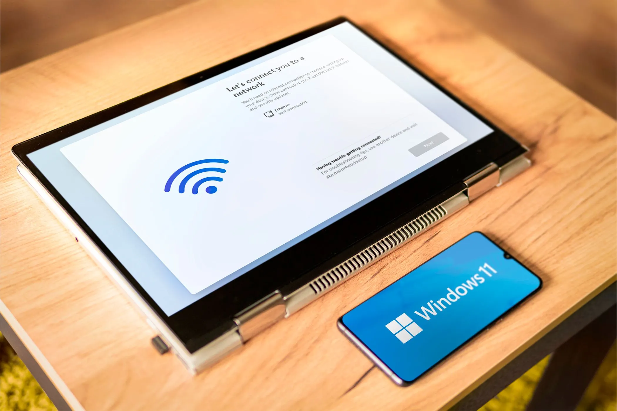 Màn hình laptop hiển thị cài đặt Windows 11 cùng điện thoại Android có logo Windows 11, minh họa khả năng sử dụng smartphone cũ làm màn hình phụ.
