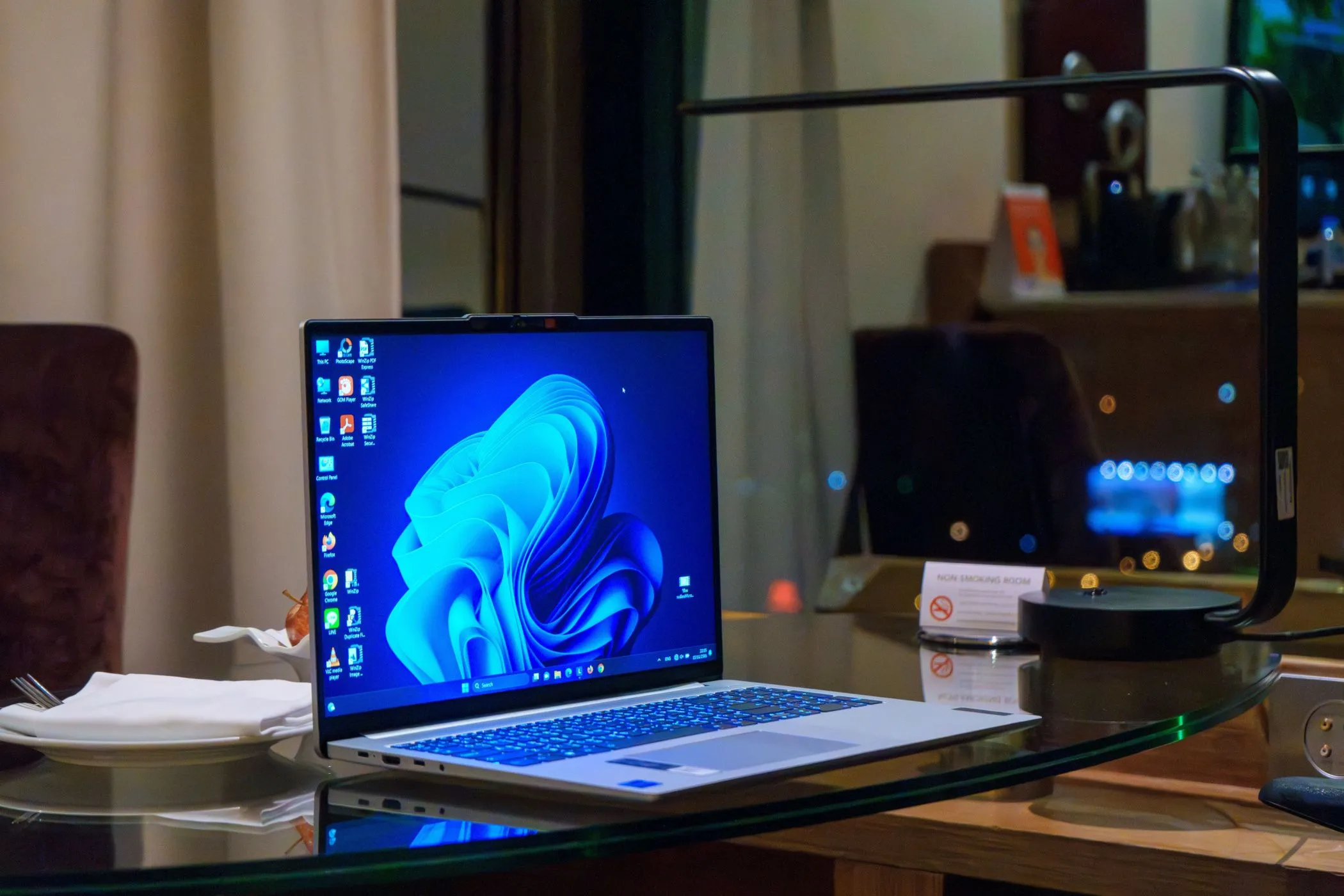 Một chiếc laptop Windows đặt trên bàn kính với các biểu tượng ứng dụng trên màn hình nền.