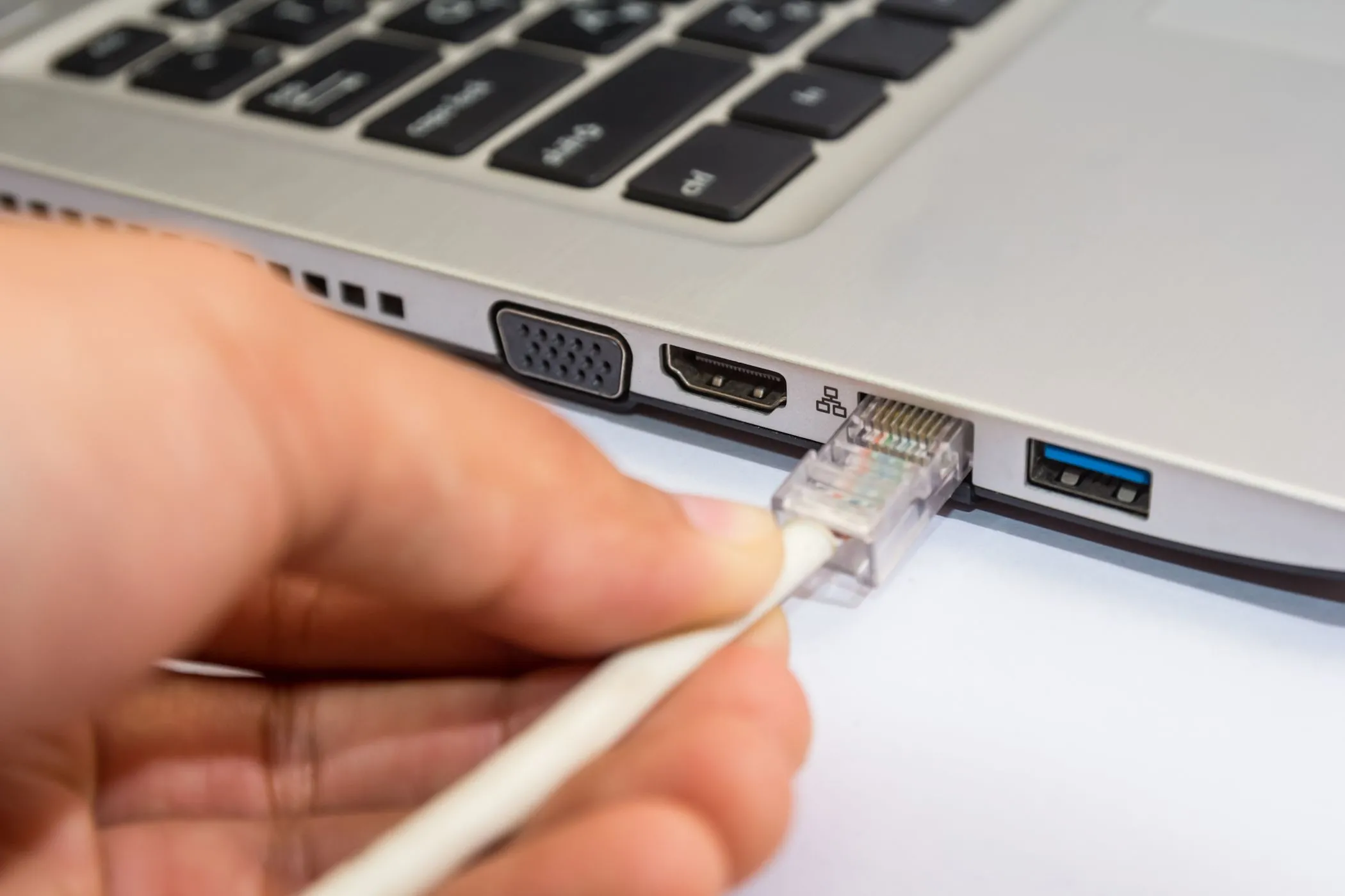 Người đàn ông đang cắm cáp Ethernet vào máy tính xách tay chạy Windows, minh họa kết nối mạng dây an toàn.