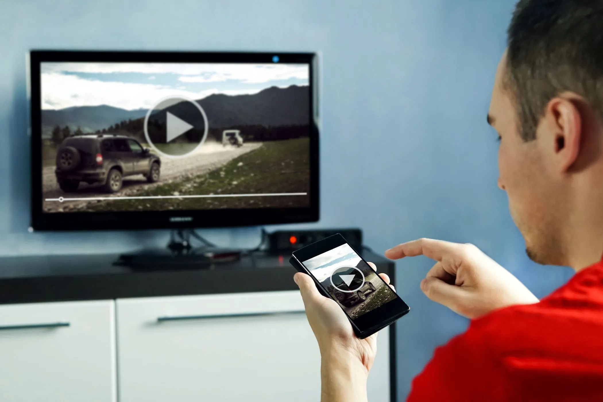Người đàn ông xem video trên TV thông minh và sử dụng ứng dụng điều khiển qua điện thoại