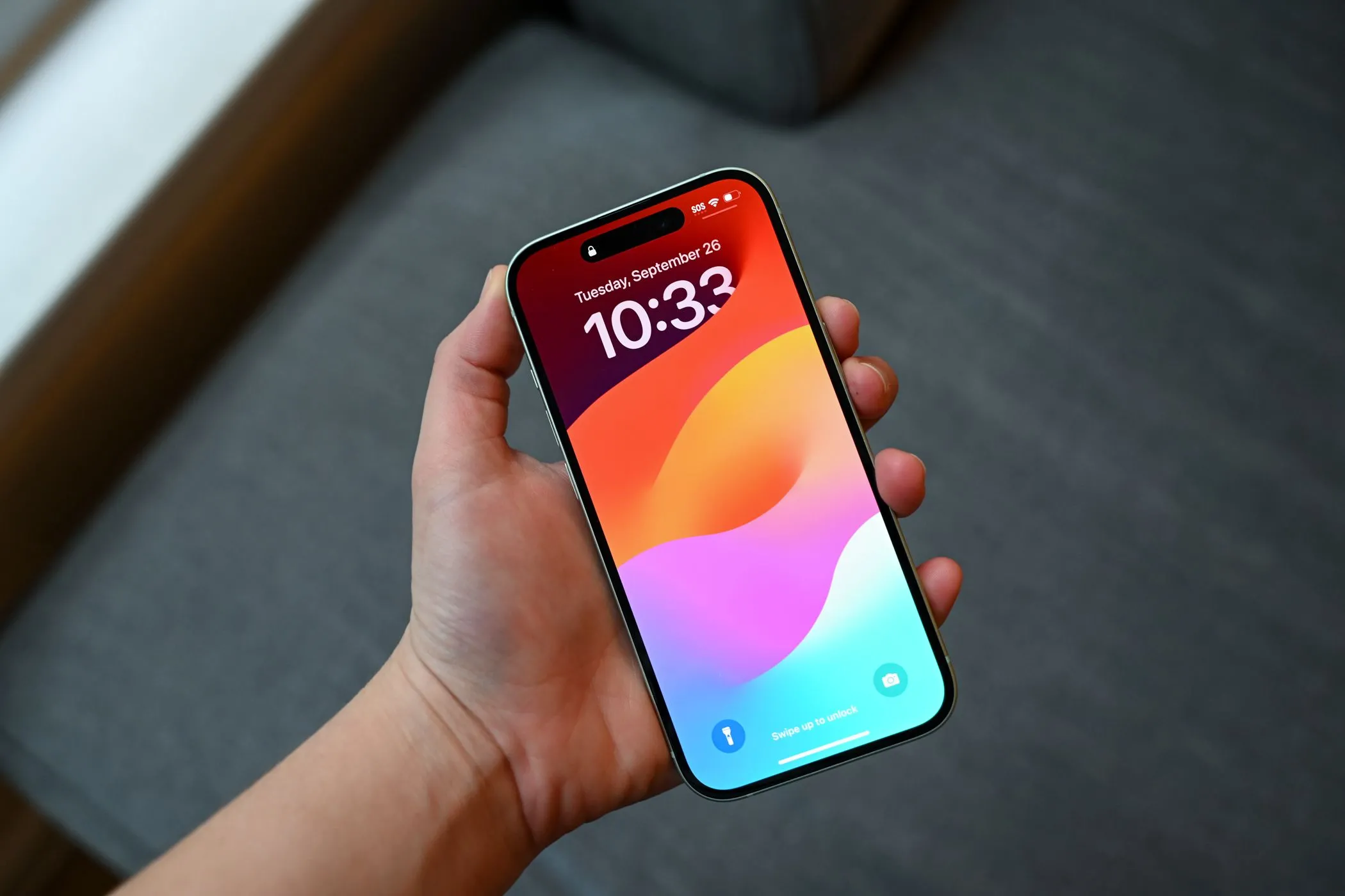 Người dùng cầm iPhone 15 đang hiển thị màn hình khóa, minh họa khả năng che giấu vết xước của miếng dán chống nhìn trộm.