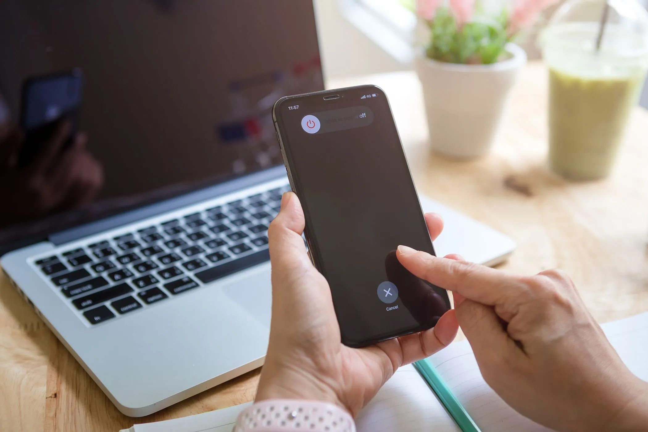 Người phụ nữ đang cố gắng tắt nguồn iPhone của mình với MacBook ở hậu cảnh, làm rõ lầm tưởng về việc tắt máy để tăng tốc độ sạc pin.
