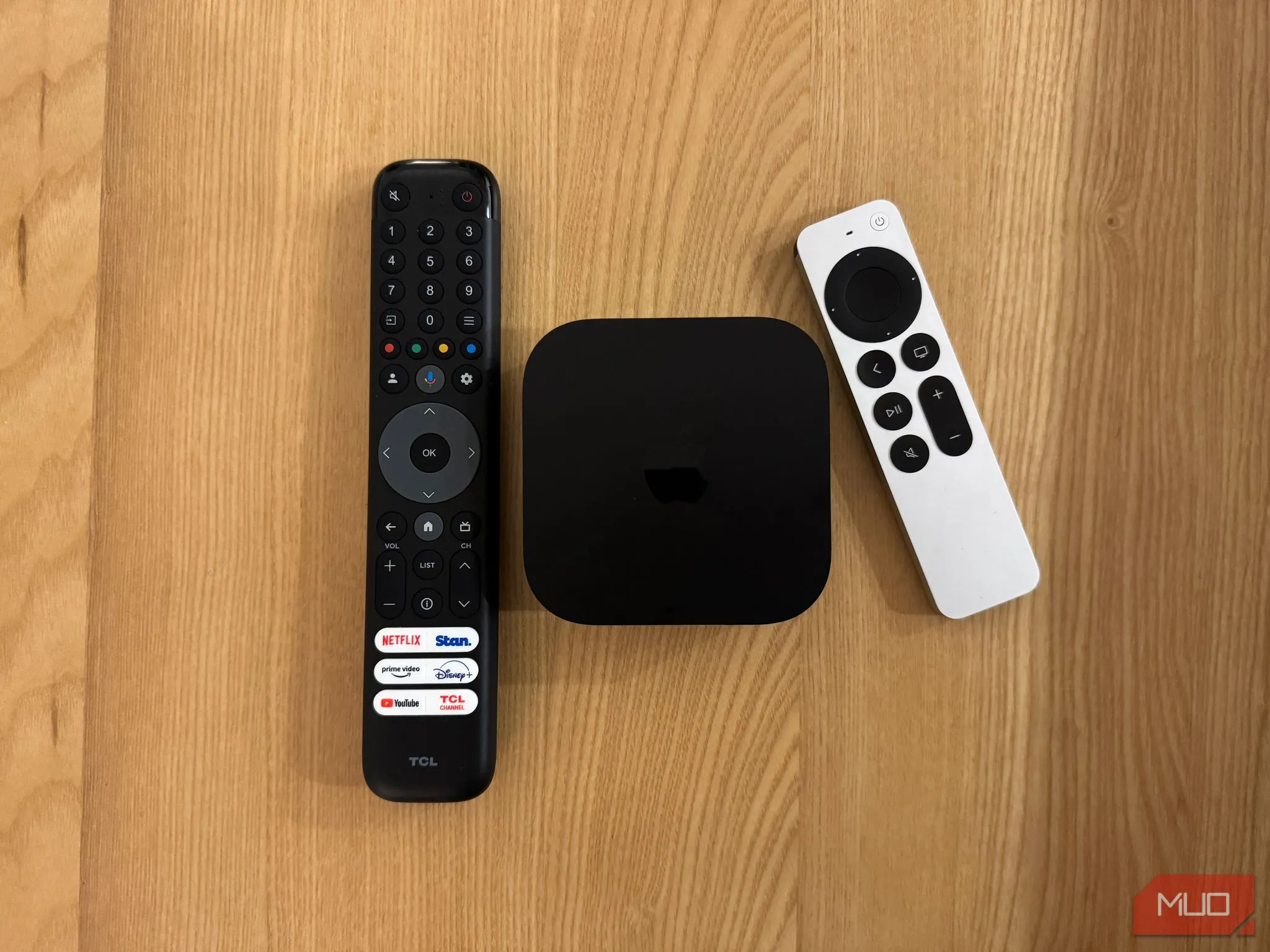 Siri Remote của Apple TV 4K với thiết kế nhôm cao cấp, đặt cạnh Apple TV và một điều khiển TV thông thường, cho thấy sự khác biệt về chất lượng.
