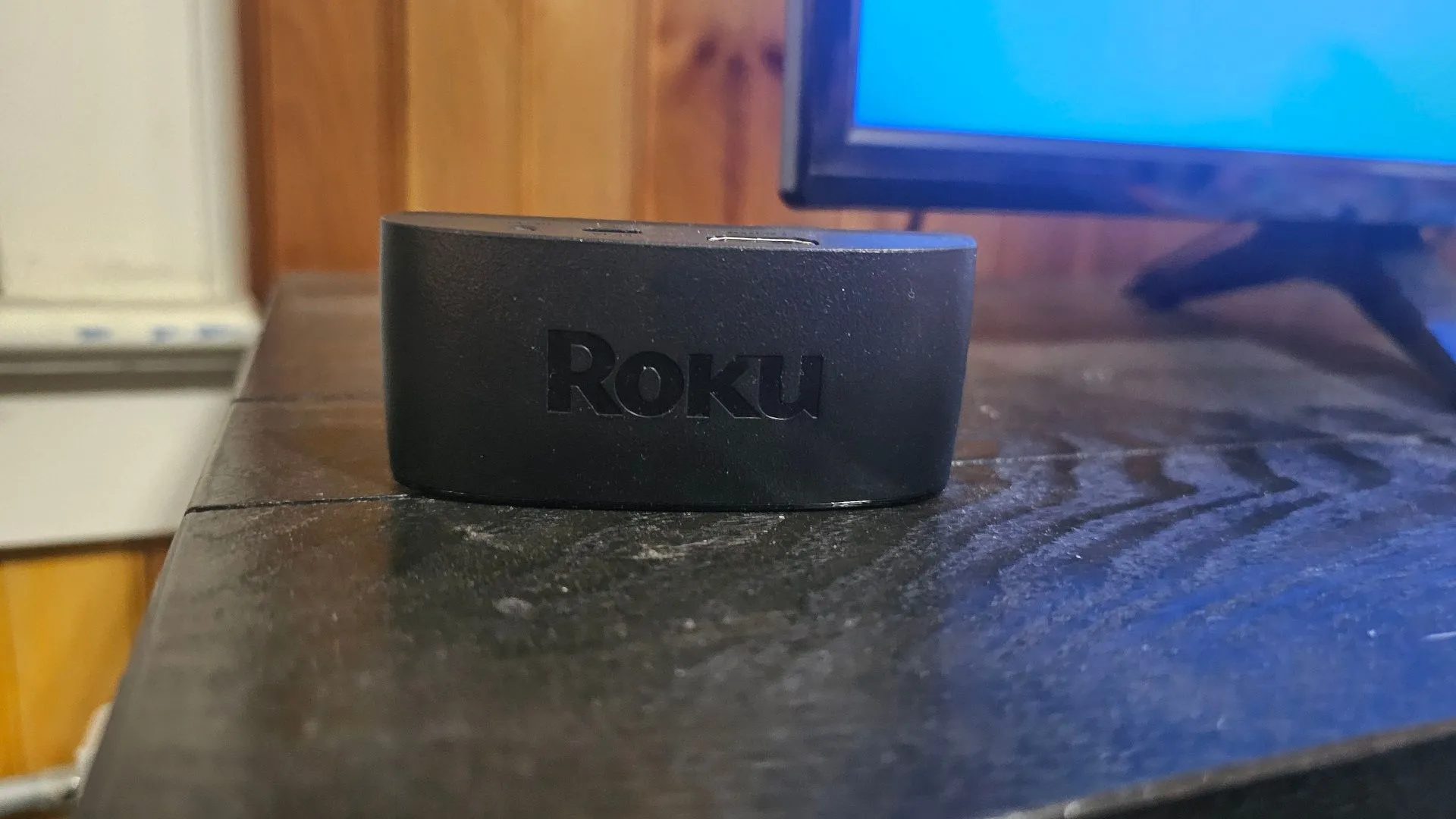 Thiết bị Roku Streaming Device trên kệ TV, gần màn hình.